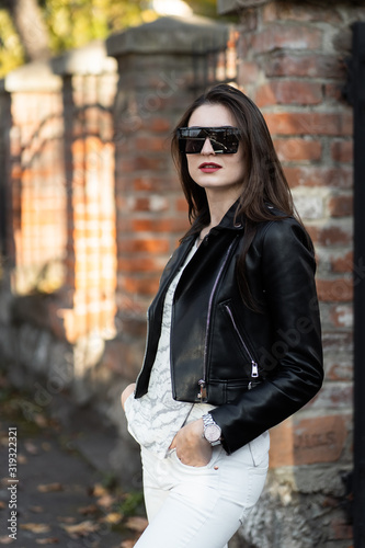 Obraz na płótnie Outdoor fashion portrait of stylish young woman having fun, emotional face , laughing, Urban city street style.Girl wearing white pants,t-shirt, black leather jacket , sunglasses and dark hat Fashion. w salonie