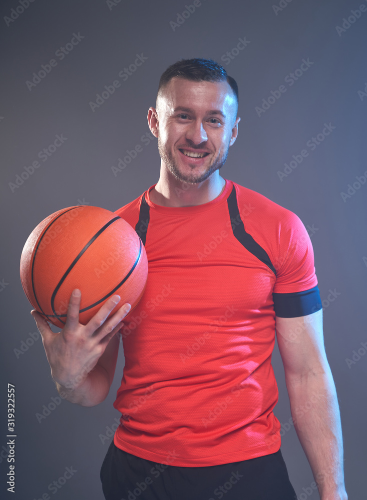 Young athletic man posing holding basketball ball with one hand in front of grey smoky background Young athletic man posing holding basketball ball with one hand in front of grey smoky background