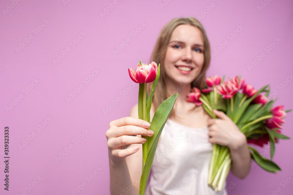 attractive girl holds a bouquet of flowers on a pink background and gives one tulip, the seller offers flowers, a woman gives tulips