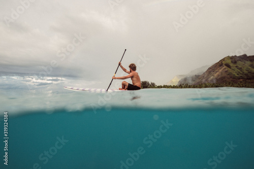 Young man paddle boards around tropical water on vacation