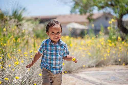 A happy, two year old boy running around and holding a flower he picked from the nearby garden.