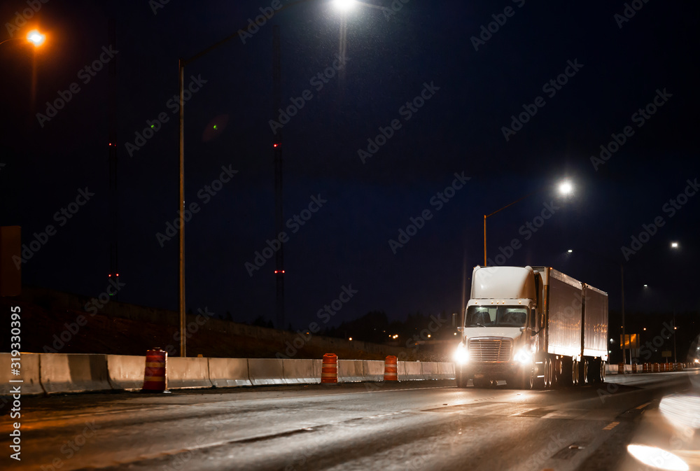 Big rig day cab semi truck transporting cargo in two semi trailers running on the wet after rain highway road at dark night time