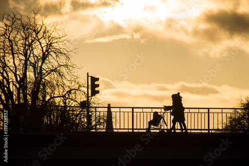 Silhouette of women with child in trolley walking on bridge by sunset