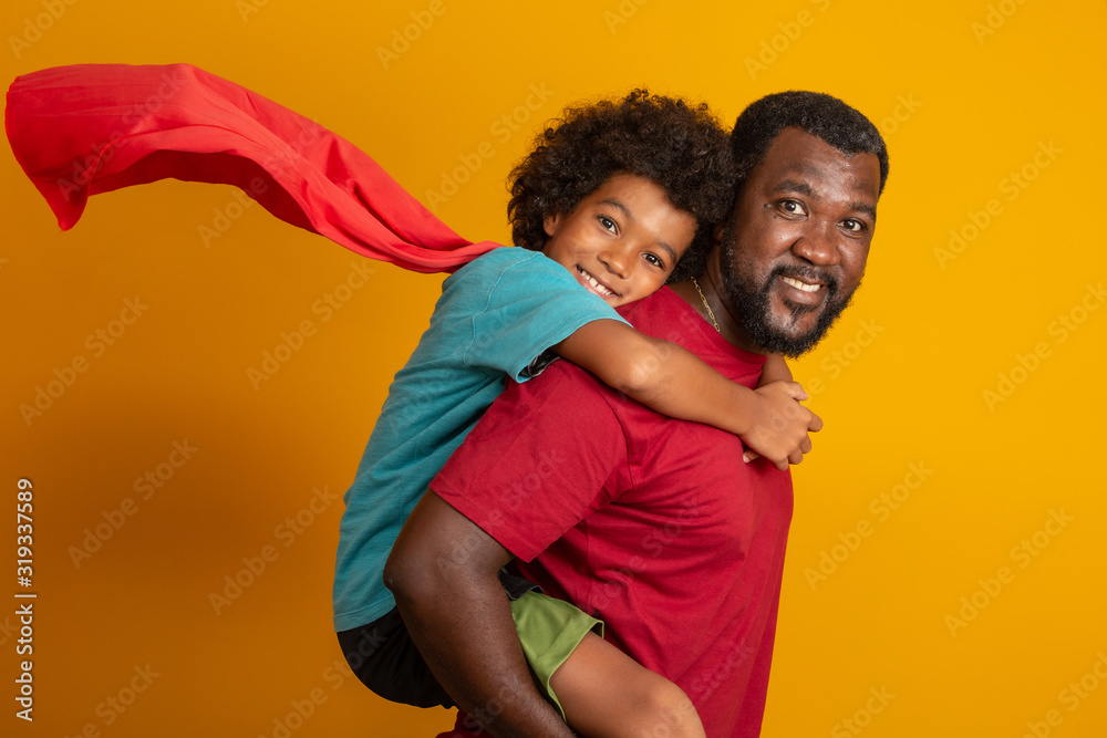 African Father and Son playing Superhero at the day time. People having fun yellow background. Concept of friendly family. - obrazy, fototapety, plakaty 