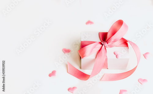 White gift box with pink ribbon and a small pink hearts on white background. Selective focus. Copy space
