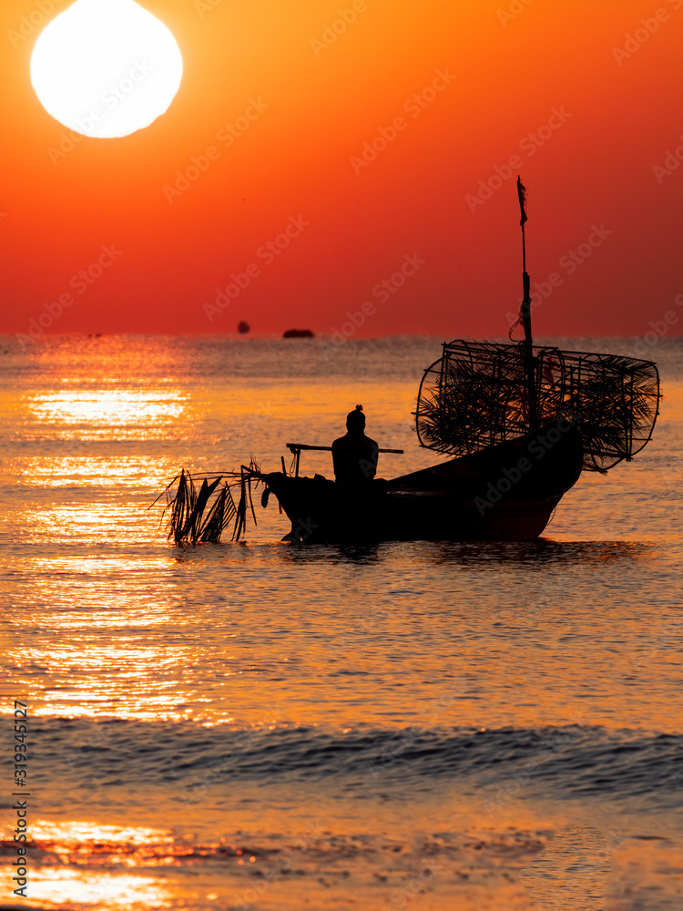 Silhouette of a traditional Thai fishing boat with a background of the golden glow of sunrise and the reflections of the rising sun on the water.