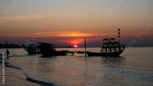 Silhouette of a traditional Thai fishing boat with a background of the golden glow of sunrise and the reflections of the rising sun on the water.