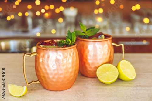 Two slylish Moscow mule cocktails in metallic cups with lemon and mint on bar stand. with festive bokeh lights effect photo