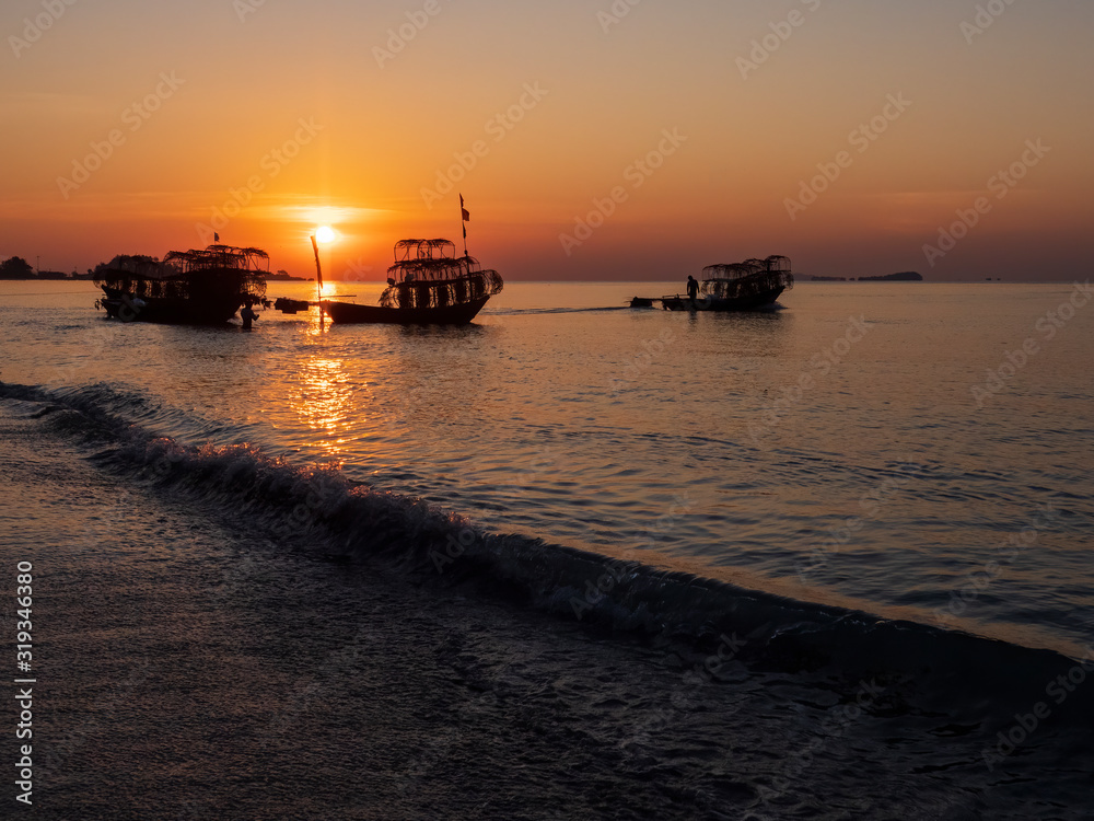 Silhouette of a traditional Thai fishing boat with a background of the golden glow of sunrise and the reflections of the rising sun on the water. Silhouette of a traditional Thai fishing boat with a background of the golden glow of sunrise and the reflections of the rising sun on the water.