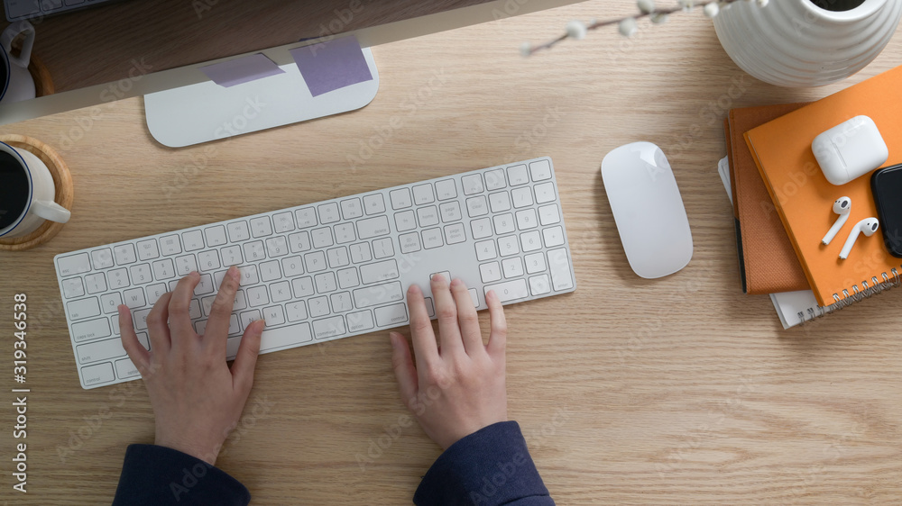 top view of freelancer typing on computer keyboard in workspace with other office supplies on wooden desk top view of freelancer typing on computer keyboard in workspace with other office supplies on wooden desk