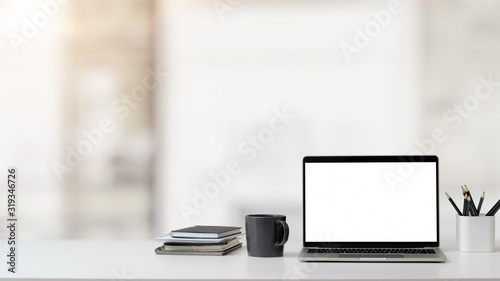 Close up view of workspace with laptop, office supplies and coffee cup on white table with blurred background