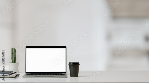 Close up view of workspace with laptop, office supplies, coffee cup and cactus pot on white table with blurred background