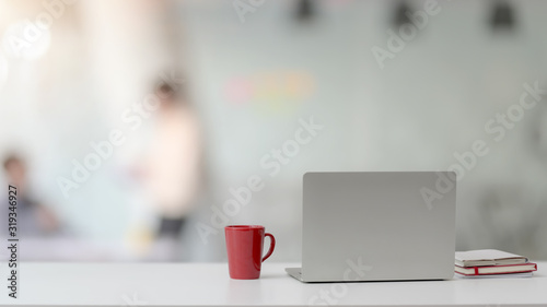 Close up view of workspace with laptop, notebooks, red coffee cup and copy space on white desk