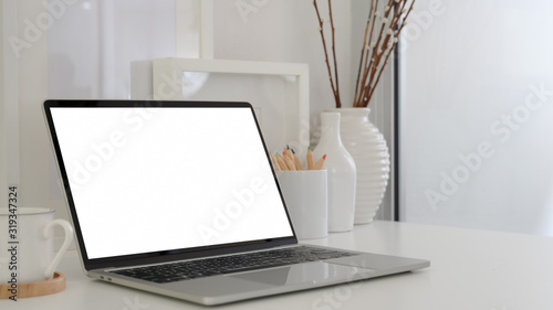 Cropped shot of modern workspace with blank screen laptop, coffee cup and ceramic decorations