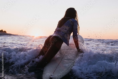 Young girl paddles out on surfboard at sunset photo