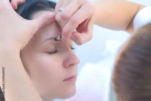 Cosmetologist painting shape of eyebrows for client woman before microblading procedure, side view, face closeup. Beautician preparing patient to beauty procedure. Young girl in beauty clinic.