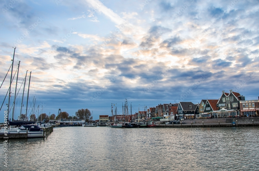 Fishing boats and yachts moored in marina in front of the traditional dutch wooden fishing houses in Volendam, Netherlands