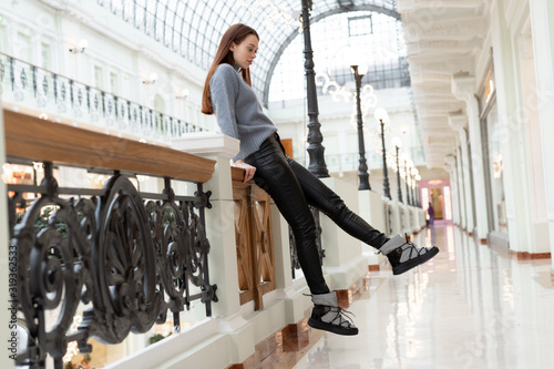 Caucasian model girl in black leather pants, gray uggs and a fluffy sweater posing indoors