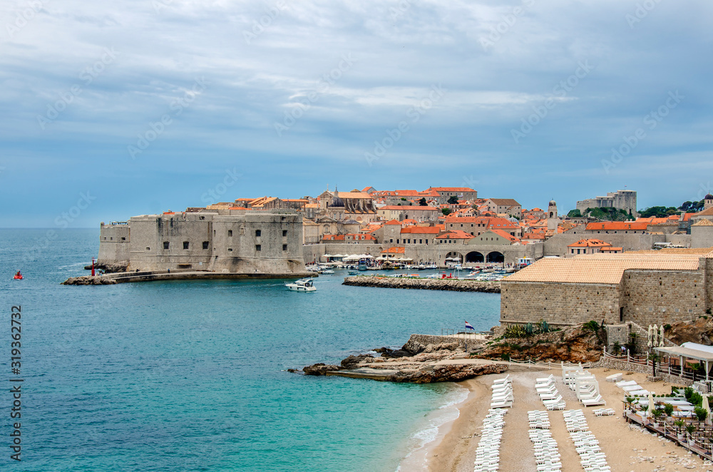 View of Dubrovnik fortress walls, beach and turquoise water. Famous Banje Beach with view of the Dubrovnik city walls and old town. Beautiful blue water and yellow send.