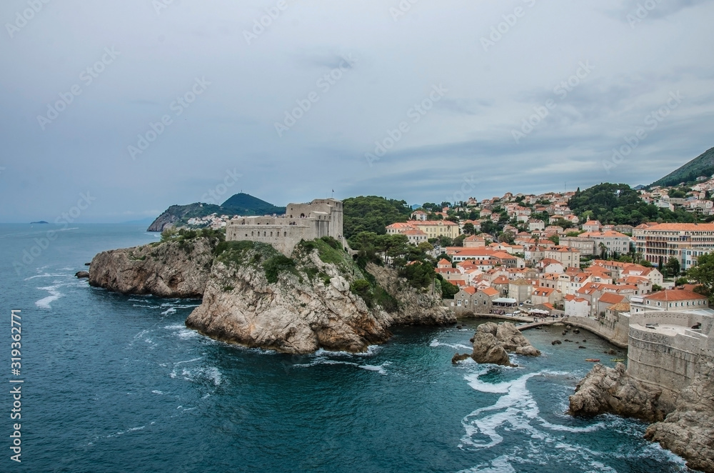 View of city walls of Dubrovnik and blue sea, Dubrovnik, Croatia. Dubrovnik old town surrounded by old walls. View from above of red rooftops, roofs and fortress.