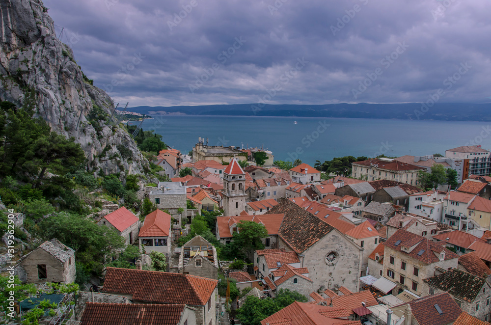 Aerial panoramic view of the small town Omis surrounded with mountains, Cetina river and sea, Makarska Riviera, Croatia. View of pine tree,  old city center with red rooftops and blue see.