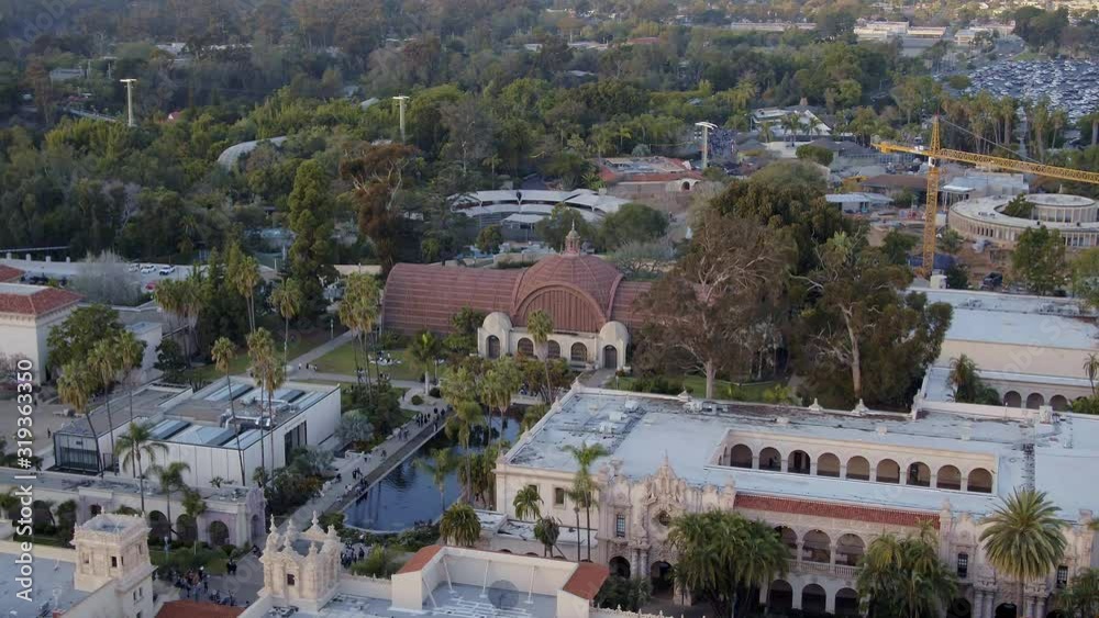 Aerial drone footage of the iconic buildings and towers of Balboa Park during a beautiful Sunset with the San Diego, California skyline is the background. 