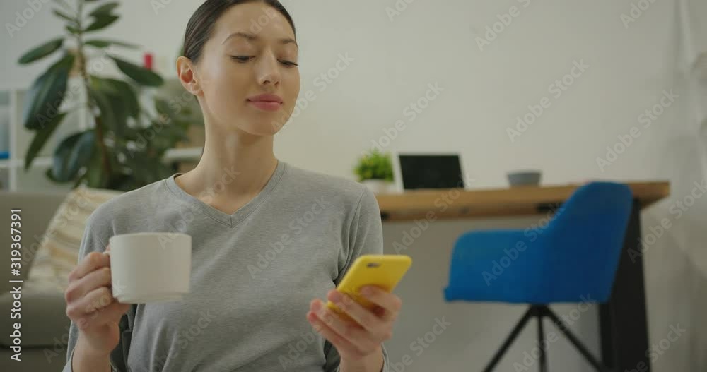 athletic young woman reading message, smiling and looking at the camera with a cup of tea in her hand athletic young woman reading message, smiling and looking at the camera with a cup of tea in her hand
