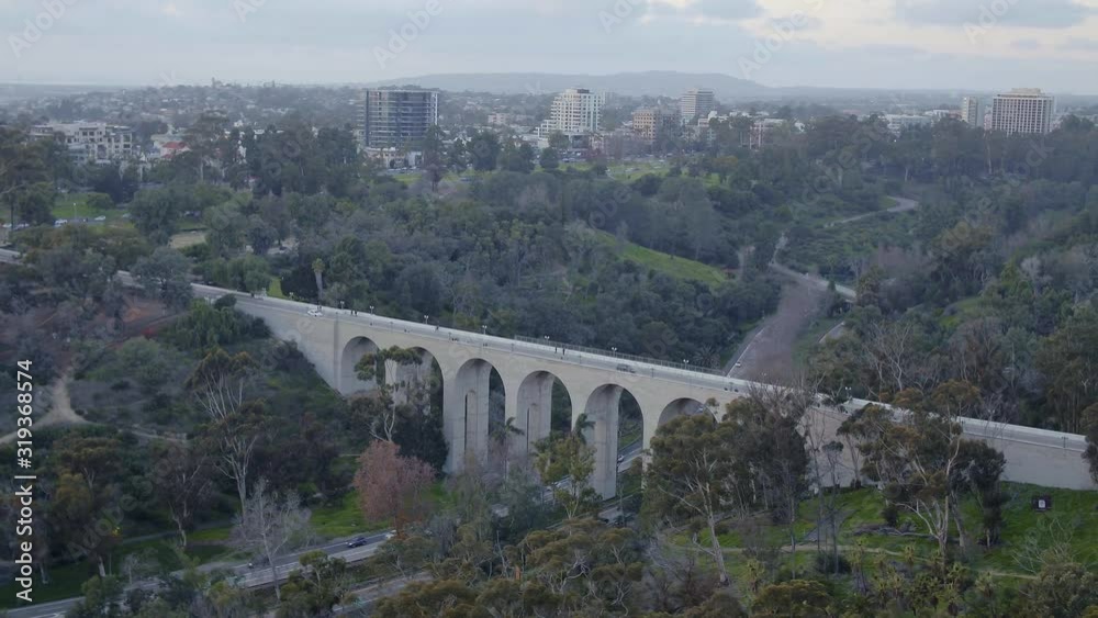 Aerial drone footage of the iconic buildings and Cabrillo Bridge of Balboa Park during a beautiful Sunset with the San Diego, California skyline is the background. 