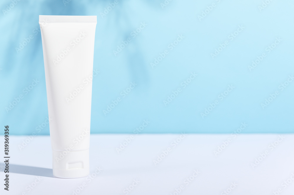 Feminine hygienic product tube on sunny blue background with leaf shadow. Shampoo, hand cream, toothpaste white package side view. Skincare, facial creme, moisturizer container with place for text Feminine hygienic product tube on sunny blue background with leaf shadow. Shampoo, hand cream, toothpaste white package side view. Skincare, facial creme, moisturizer container with place for text