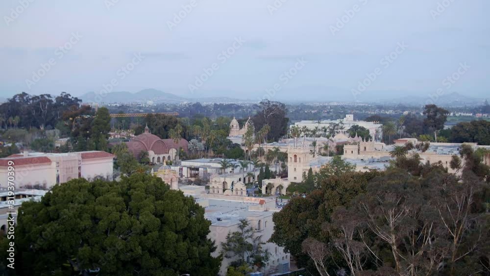 Aerial drone footage of the iconic buildings and towers of Balboa Park during a beautiful Sunset with the San Diego, California skyline is the background. 