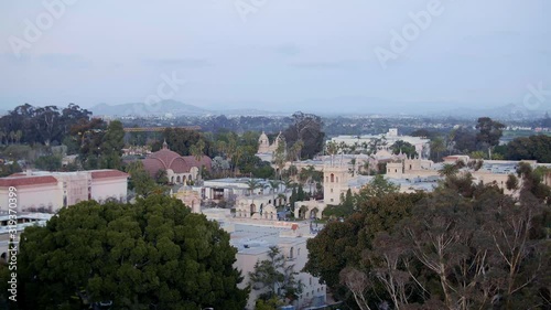 Aerial drone footage of the iconic buildings and towers of Balboa Park during a beautiful Sunset with the San Diego, California skyline is the background.  photo