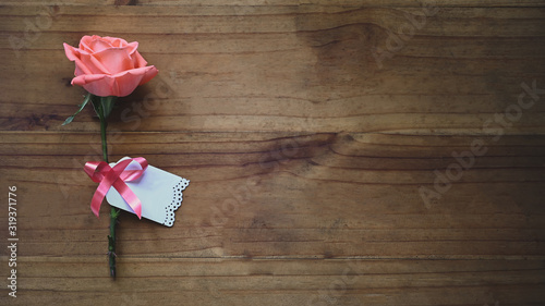Top view image of pink rose and wishes card tied together with red ribbon all of these putting on the wooden table. Surprising Valentine's Day gift concept.