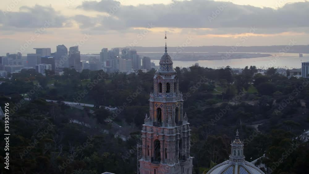 Aerial drone footage of the iconic buildings and towers of Balboa Park during a beautiful Sunset with the San Diego, California skyline is the background. 