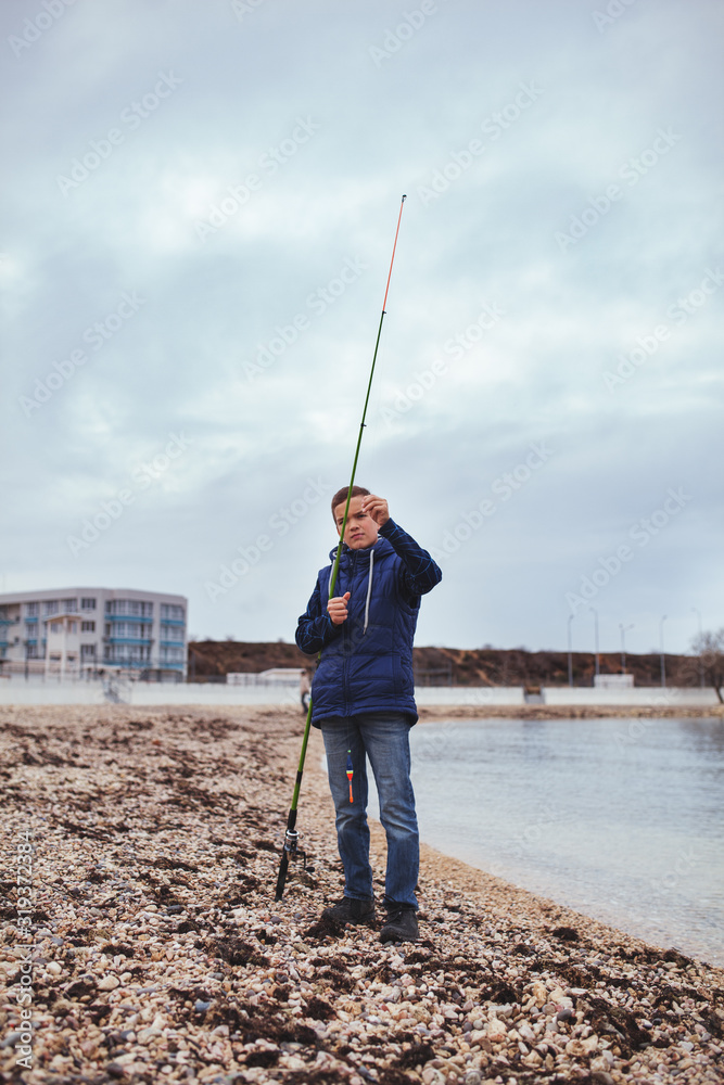 Boy with a fishing rod catches fish standing on the bank of the sea