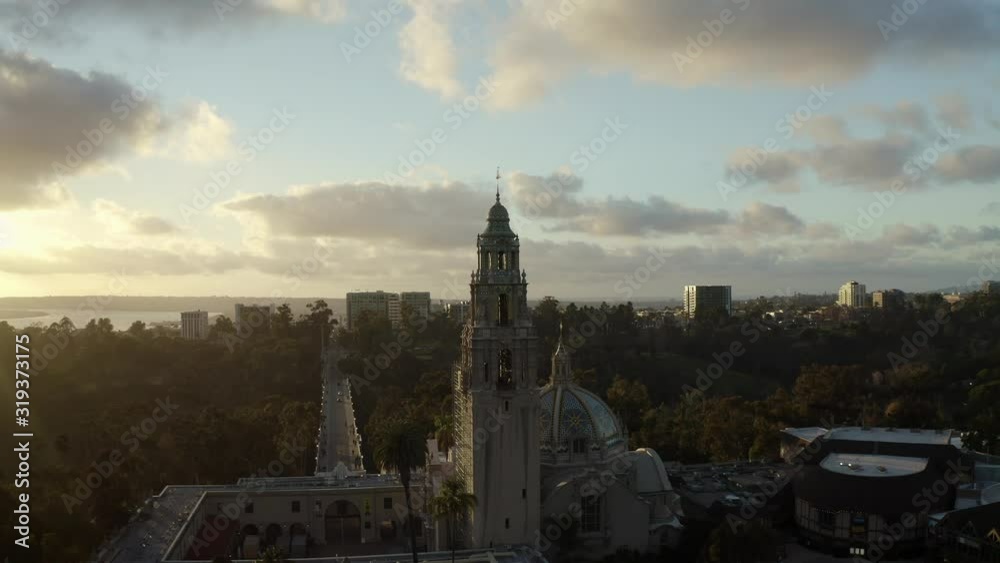 Aerial drone footage of the iconic buildings and towers of Balboa Park during a beautiful Sunset with the San Diego, California skyline is the background. 