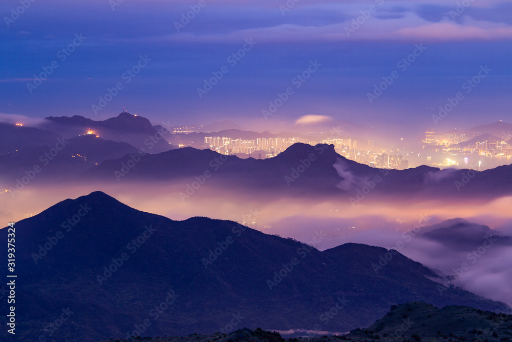 Lion Rock setting on of colourful clouds just before sunrise, with the lights of Hong Kong city in behind.