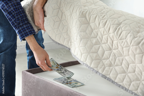 Принти на полотні Man hiding dollar banknotes under mattress in bedroom, closeup