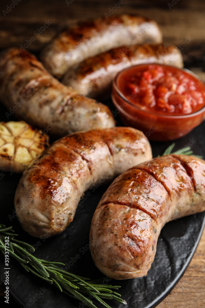 Tasty grilled sausages served with sauce on wooden table