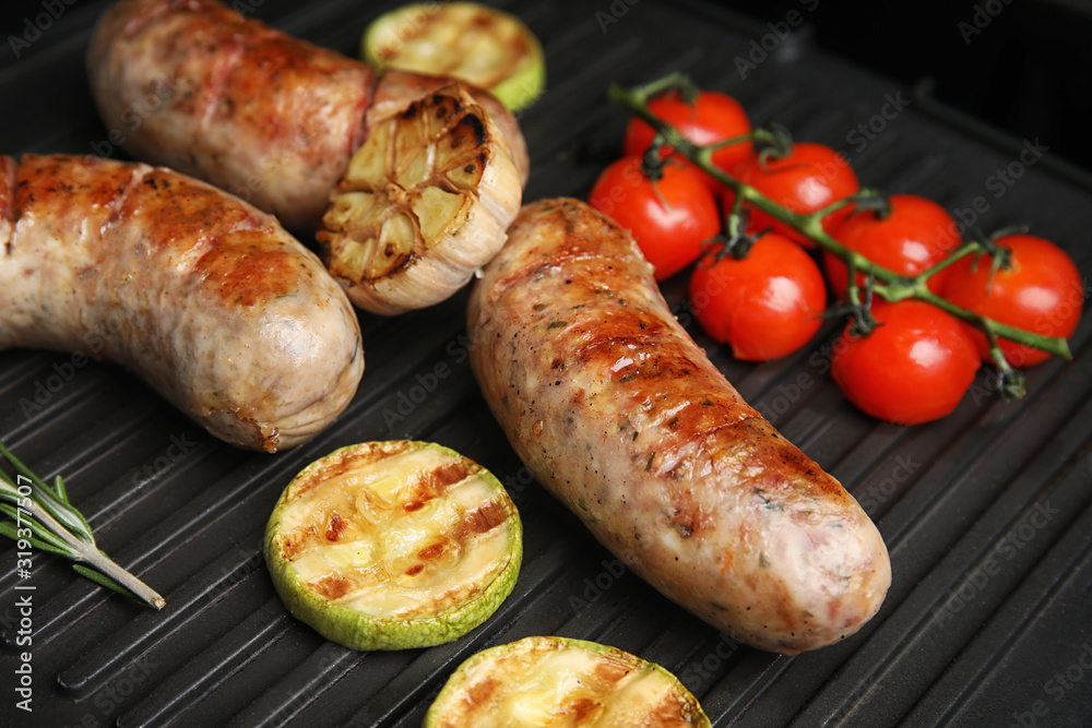 Cooking delicious fresh sausages with vegetables on modern grill Cooking delicious fresh sausages with vegetables on modern grill