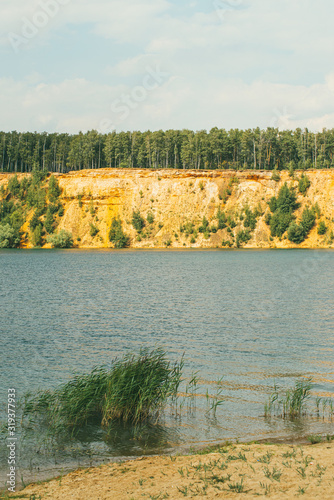 High rocky sandy steep bank covered with pine trees over a clear and blue lake