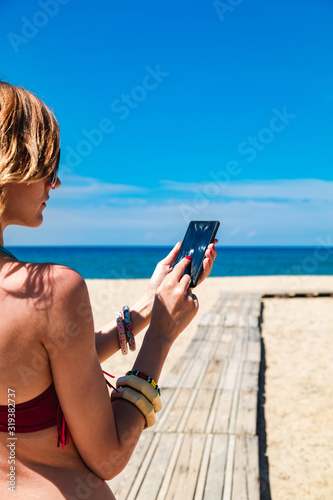 Young woman using cellphone on a tropical sandy beach.