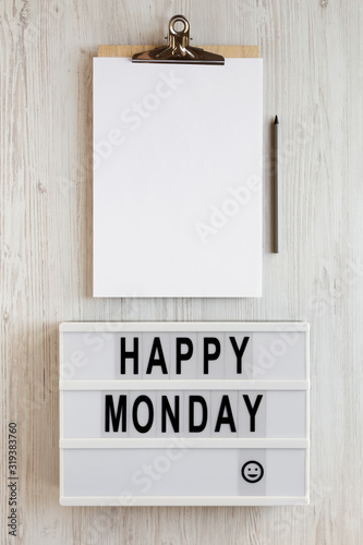 'Happy monday' words on a lightbox, clipboard with blank sheet of paper on a white wooden surface, top view. Overhead, from above, flat lay. Close-up. photo