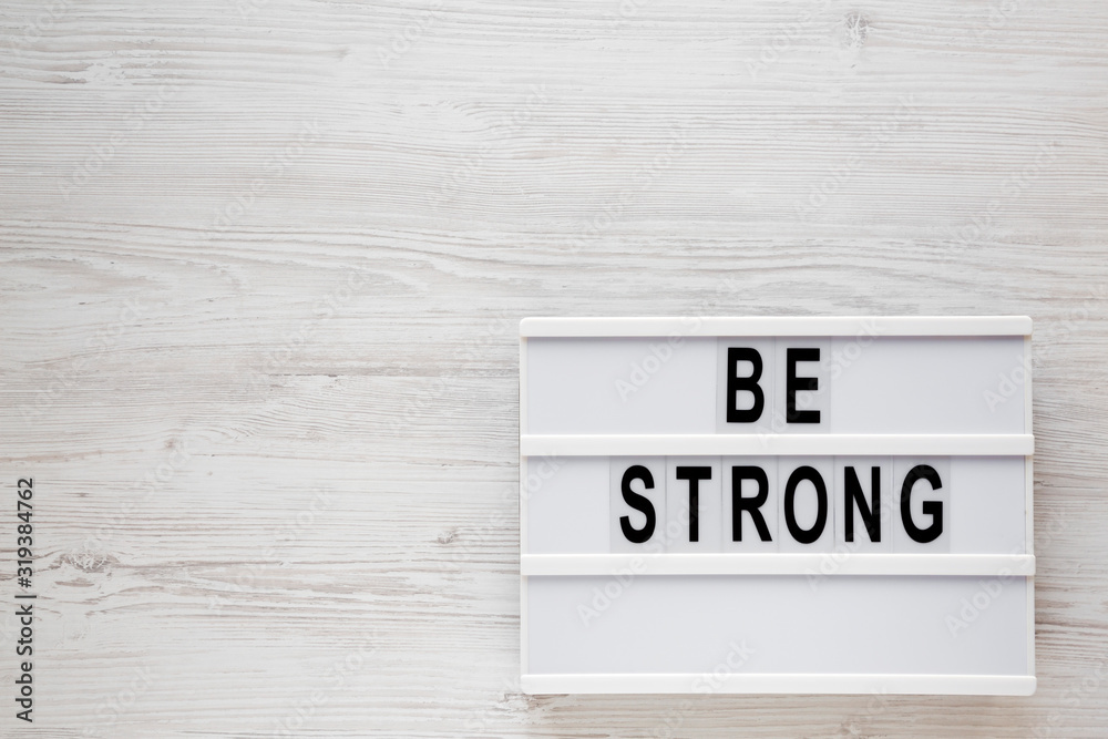 'Be strong' words on a lightbox on a white wooden background, top view. Overhead, from above, flat lay. Space for text.