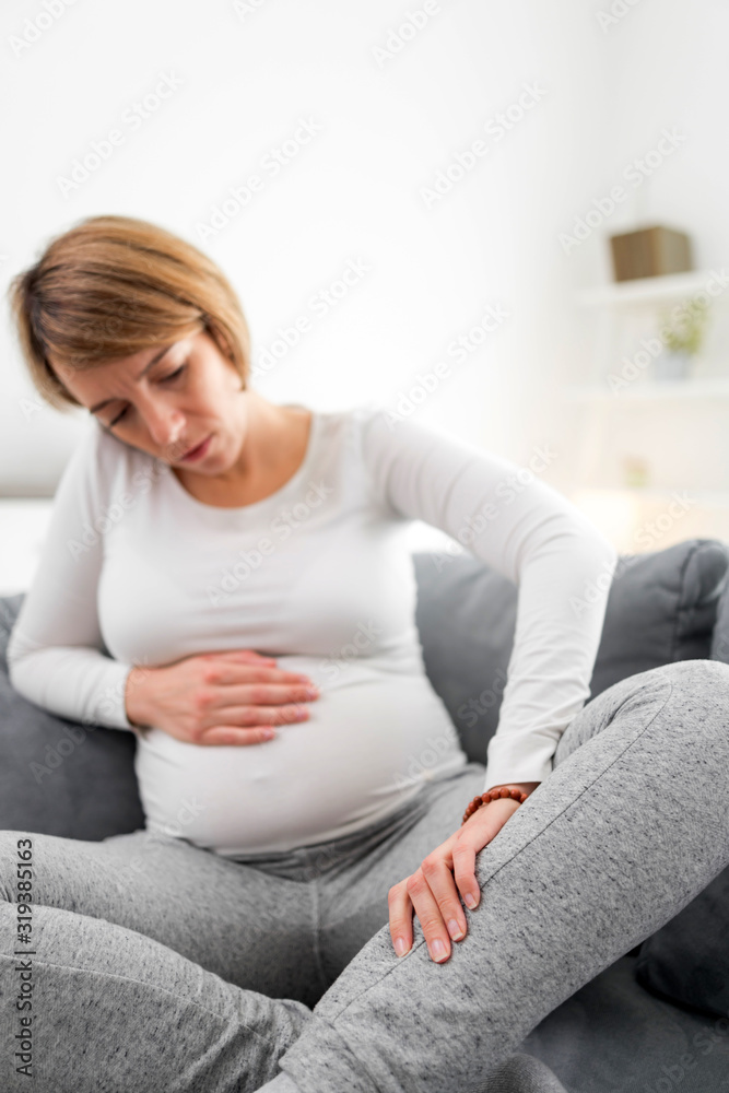 Pregnant tired exhausted woman with stomach, leg and pain issues at home on a couch, being sick. Pregnant tired exhausted woman with stomach, leg and pain issues at home on a couch, being sick.