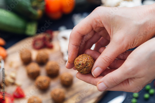 Female hands preparing raw vegan meat balls on a dark table top.