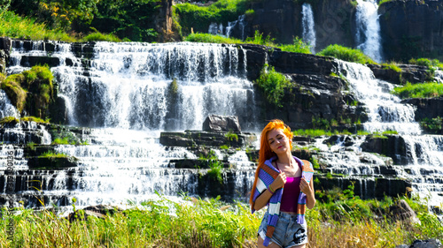 Beautiful young red haird girl staying near amazing  waterfall in Da Lat city Vietnam.Traveler girl with long red hair looking to beautiful Pongour  waterfall. photo