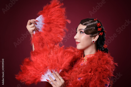 Beautiful asian woman wearing red traditional vintage chinese dress holding feather fan on red background, Thailand