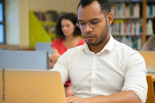 Focused man typing on laptop. Handsome young student sitting at library and using modern device. Technology concept