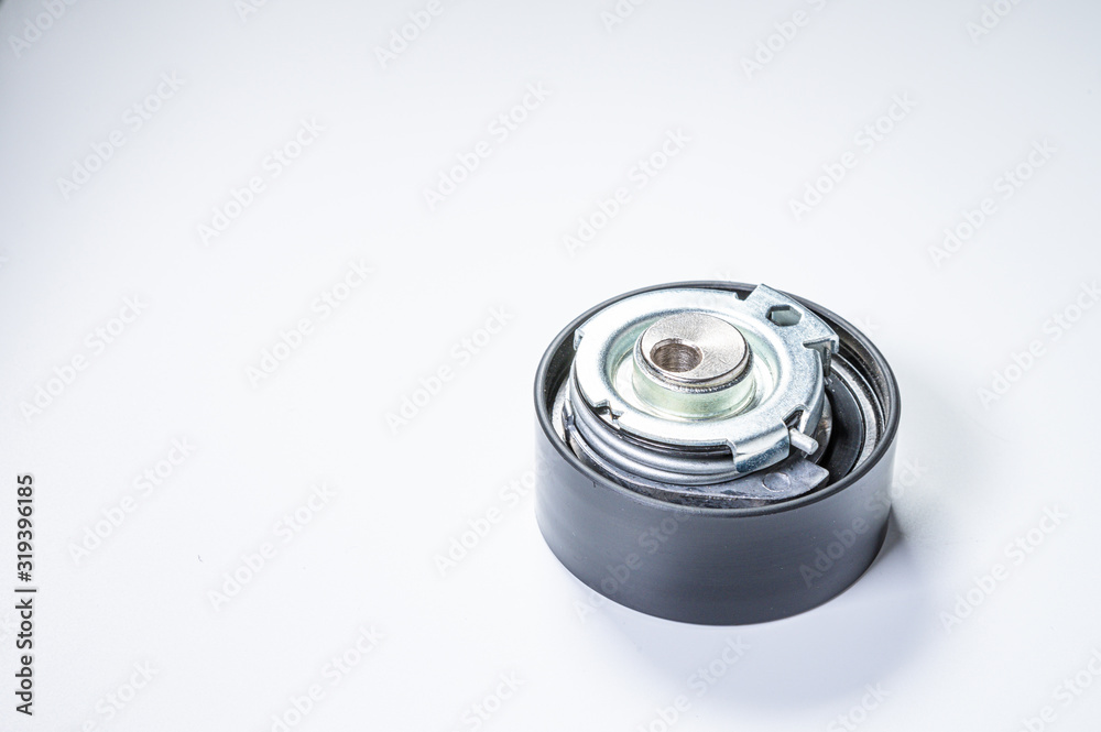 Tension roller of a timing belt of an internal combustion engine on a gray background. The concept of new spare parts and maintenance of vehicles Tension roller of a timing belt of an internal combustion engine on a gray background. The concept of new spare parts and maintenance of vehicles