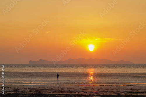 view seaside evening of a man walking on sand beach with sundown and orange sun light in the sky background  sunset at Chao Mai Beach  Chao Mai National Park  Trang Province  southern of Thailand.